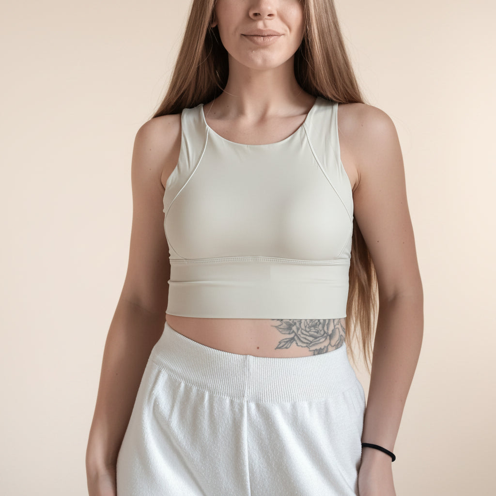 Woman wearing a beige sports bra and white pants against a plain background